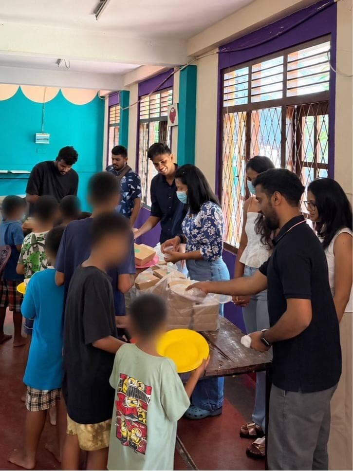 Coderra team members from Australia and Sri Lanka serving meals from a table to children queuing with plates, children's faces blurred for privacy.